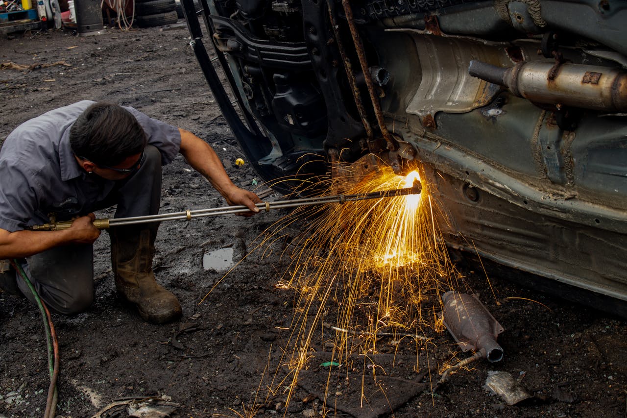 about-02 Mechanic welding a car frame outdoors, producing dramatic sparks and intense focus.