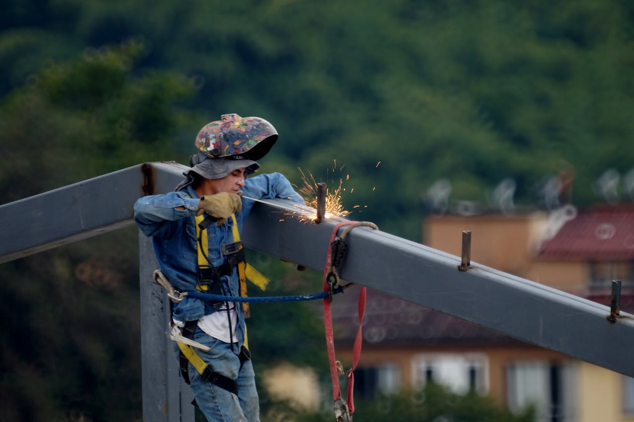 hero-img-01 Construction worker welding steel beam on site, wearing safety gear and helmet.
