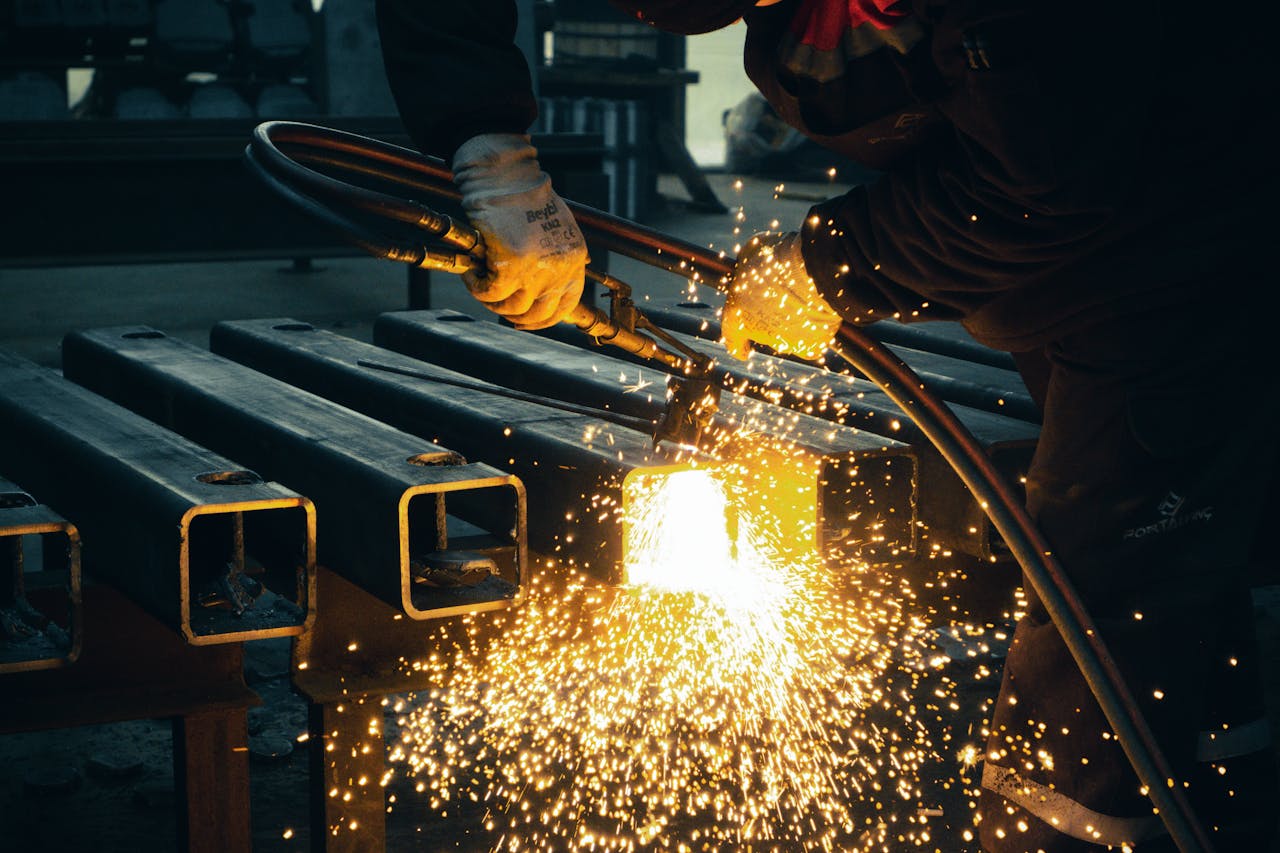 ours-journey A welder sparks metal beams indoors in an industrial factory setting.
