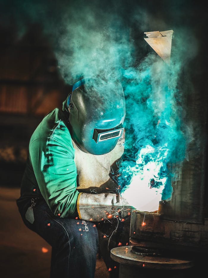 gallery-2 A skilled worker welds metal indoors, producing bright sparks and vivid colors.