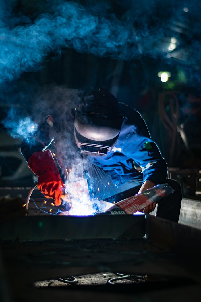 The Art of Drawing Readers In: Your attractive post title goes here A welder engaged in intense work, surrounded by sparks and smoke, creating a dramatic industrial atmosphere.