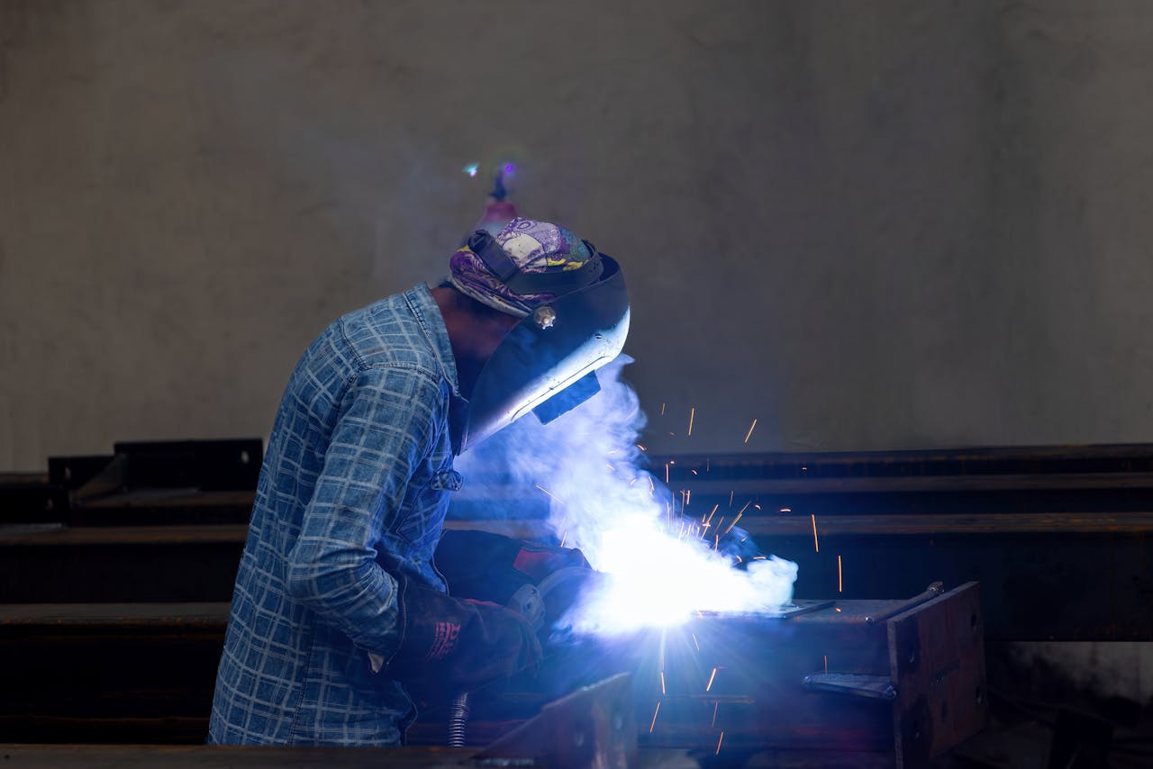 services-img A welder in protective gear working with sparks in an industrial factory environment.