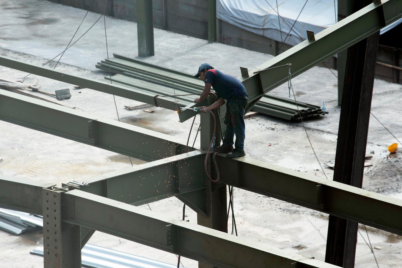 services-03 A construction worker welding steel beams on a high-rise construction site. Sparks fly as the worker welds.