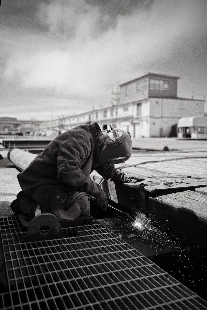 gallery-6 A welder in protective gear working on a metal structure outdoors, showcasing industrial labor.