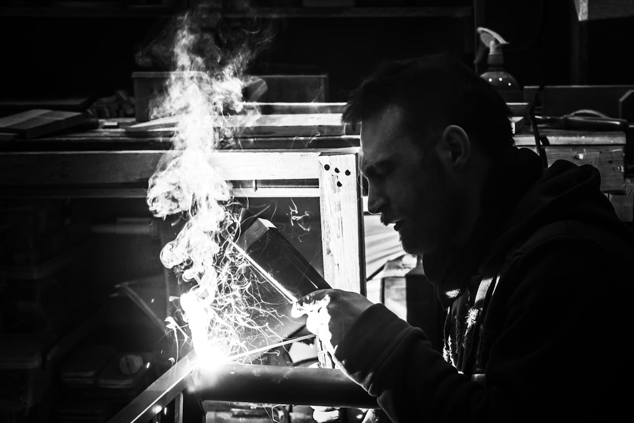 services-04 A grayscale image of a welder at work, capturing sparks and smoke in a workshop.